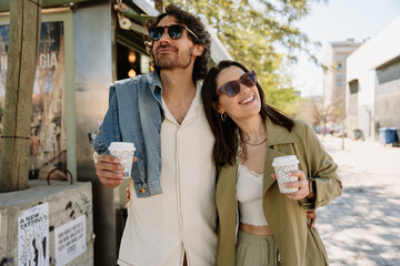 A man and a woman are hugging and holding cups while walking and smiling