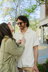 Fototapeta premium A woman buttons the shirt of a man standing next to her while they smile
