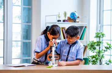 Uniformed Indian students examine plant samples under microscope and take notes in science class