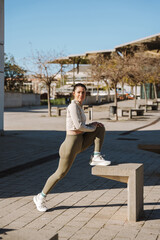 Fototapeta premium A woman warms up and stretches while resting her foot on a stone stool