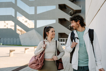 Male and female athletes smiling and looking at each other while walking and holding backpacks