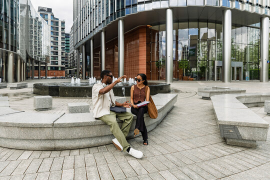A man and a woman worker sit on a stone bench and talk while he gestures - Powered by Adobe