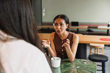 A female worker sits at a desk and talks to a female worker across from her