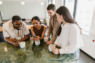 A group of four employees stand at a table and hold cups while one of them types on his phone