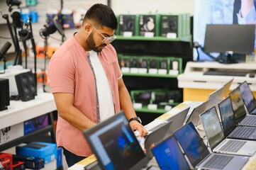 A young man stands behind his laptop at the electronics store. © Serhii