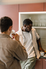 Obraz premium A male worker stands and leans on the table while taking a cup and a male worker stands opposite him who is drinking