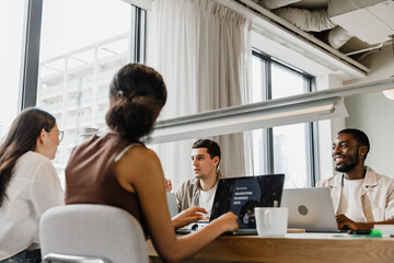 Fototapeta premium Two male workers sit at a table opposite two female workers while they listen to one of them