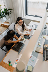A female worker smiles and looks at the folder she is holding while sitting at a table next to a...