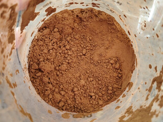 Overhead Close Up View of Rich Dark Brown Cocoa Powder or Ground Coffee in Plastic Food Ingredient Storage Container