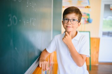 Cute little schoolboy diligent write chalk solve math problem dressed stylish uniform classroom blackboard background