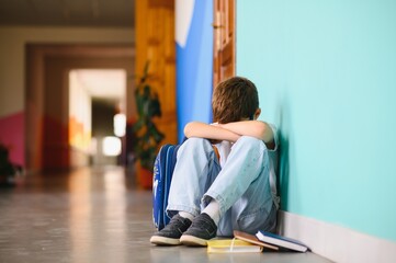 Upset boy sitting at school and crying after bullying by pupils classmates
