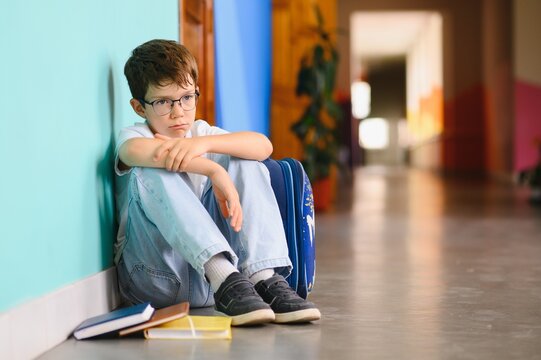 Little boy sitting alone on floor after suffering an act of bullying. Sad young schoolboy sitting on corridor with hands on knees and head between his legs