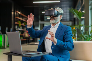 Mature businessman programmer software developer using headset app making a presentation. Watching virtual reality 3D 360 video. Bearded gray-haired guy in suit in VR goggles working at office lobby.