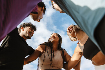 A group of five athletes laugh and hug while standing in a circle