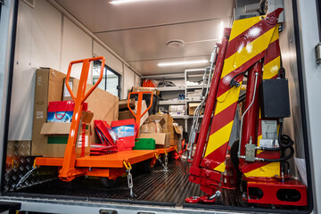 Logistics readiness: An orange pallet jack, aid boxes, and a red-yellow hydraulic crane are packed inside a utility truck, ready for deployment in humanitarian operations.