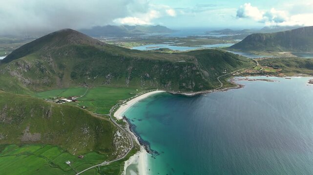 Breathtaking aerial shots capture the beauty of Mannen mountain alongside the serene Haukland beach in Lofoten, Norway. Lush green hills meet turquoise waters for a perfect landscape.