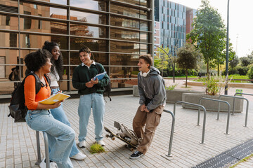 Fototapeta premium A group of four students stand and laugh while talking and two of them lean on the railing