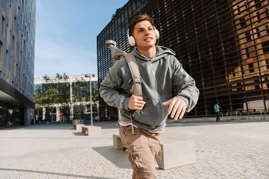 A male student is walking and holding a backpack on his shoulder while listening in headphones
