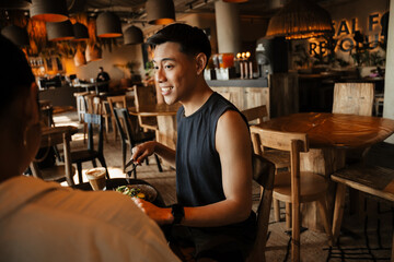 A man smiles and holds cutlery while listening to a woman sitting next to him at the table