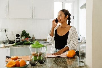 A woman is talking on the phone and standing at a table while holding a towel