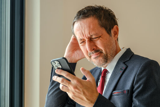 Stressed businessman reading unpleasant text message on smartphone, forgetful entrepreneur in office interior, troubled after receiving bad news at work.
