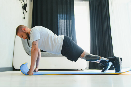 Full length portrait of man with prosthetic leg doing stretching exercises at home and reaching toes - Powered by Adobe