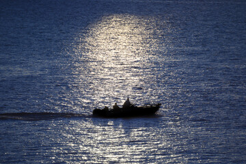 Fishing boat on the waves illuminated by the sun, silhouette of the boat.