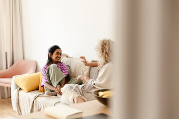 The daughter laughs and listens to her mother sitting next to her on the couch