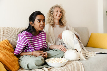 Obraz premium The daughter looks in front of her in surprise while sitting on the sofa next to her laughing mother