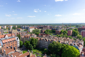 Aerial panoramic view of the historic Old Town of Gdańsk, Poland, with red tiled rooftops, bustling pedestrian street, and surrounding green landscape on a sunny summer day