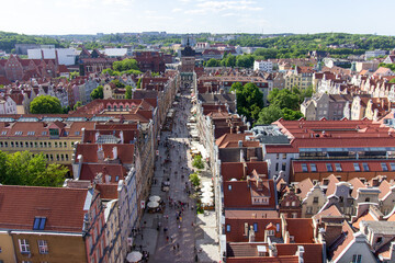 Aerial panoramic view of the historic Old Town of Gdańsk, Poland, with red tiled rooftops, bustling pedestrian street, and surrounding green landscape on a sunny summer day