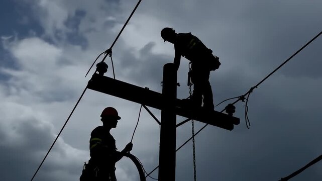 Silhouette of workers repairing power lines stormy weather