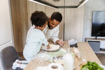 A daughter puts dough in a baking dish while standing at the table next to her laughing father