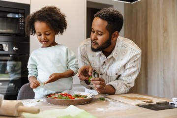 The father is talking to his daughter who is standing next to him at the table while they are holding greens
