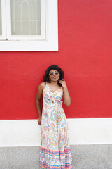 Fototapeta premium A woman is standing in front of a red wall wearing a white dress