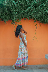 Obraz premium A woman in a long dress stands in front of a wall with green vines growing on it
