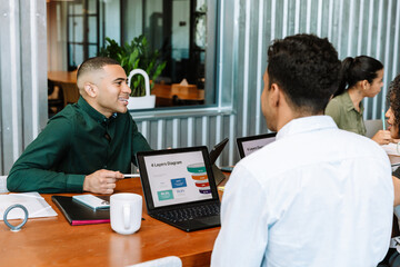 A male worker is holding a pen and smiling while sitting at a table with a group of three workers