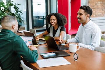 Male and female employees sitting at a table laughing while talking to the male employee across...