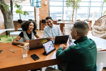 Naklejka na ściany i meble Male and female employees laughing and sitting at a table across from the male employee Naklejka na ściany i meble Male and female employees laughing and sitting at a table across from the male employee