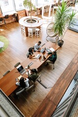 Two female workers sit at a table next to a group of three workers while they talk