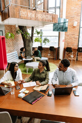 A female worker is talking to a male and female workers who are listening while they are sitting at a table