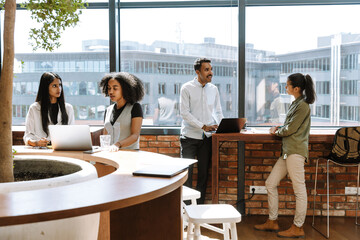 A group of four workers talking in pairs while standing at their desks