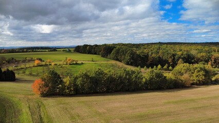 Fototapeta premium Beautiful sunny day with green fields and colorful trees on the horizon of the Czech countryside. Aerial drone view capturing the vibrant autumn landscape 