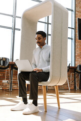Fototapeta na wymiar A male worker looks at a laptop on his lap and sits on a chair Fototapeta na wymiar A male worker looks at a laptop on his lap and sits on a chair
