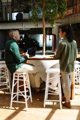 A female worker stands and talks to a male worker who is sitting at a desk and holding a pen