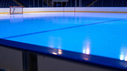 Empty indoor ice rink with blue lighting and goal net visible in the background