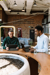 Two male workers sitting at a desk and smiling while looking at a laptop and a computer tablet