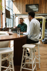 Two male workers smiling and talking while sitting at a table in front of a laptop and a computer tablet