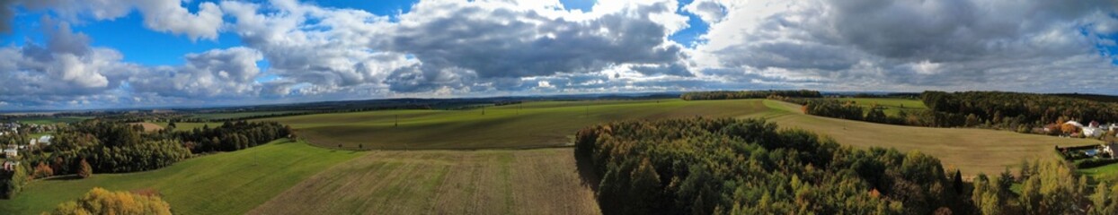 Obraz premium Panoramic aerial view of the Czech countryside on a sunny autumn day, showing green fields, forests, and a clear blue sky, captured from a drone for a scenic landscape perspective.