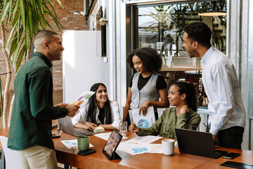 A group of five workers are laughing and talking while three of them are standing and two are sitting at a table